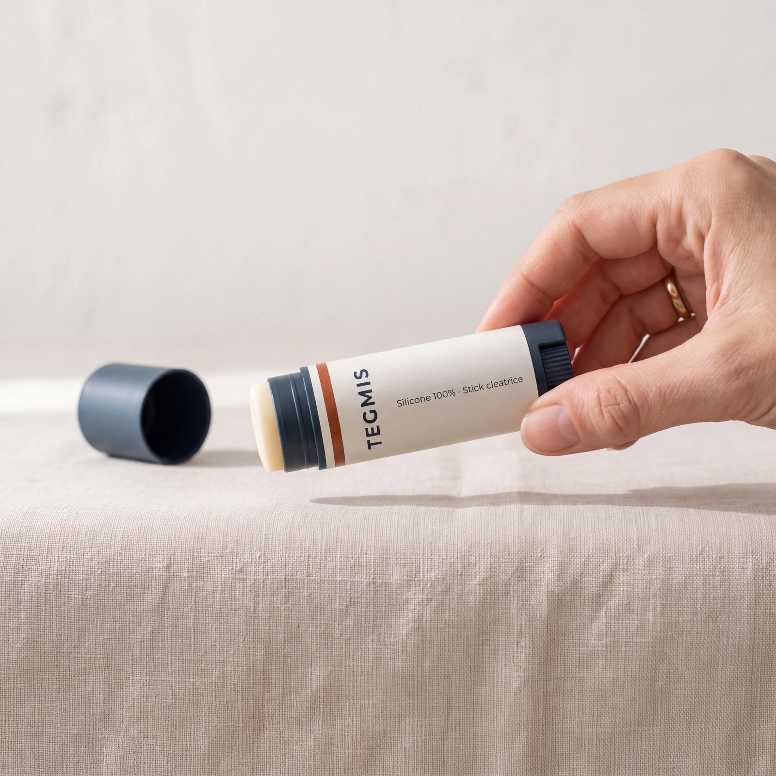IMG-02 — le stick ouvert, en suspension juste au-dessus d’un pli du lin, sans le toucher.